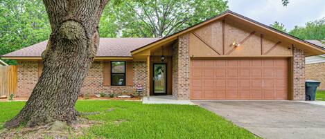 A residential house with a brick exterior, a garage, and a large tree in the front yard.