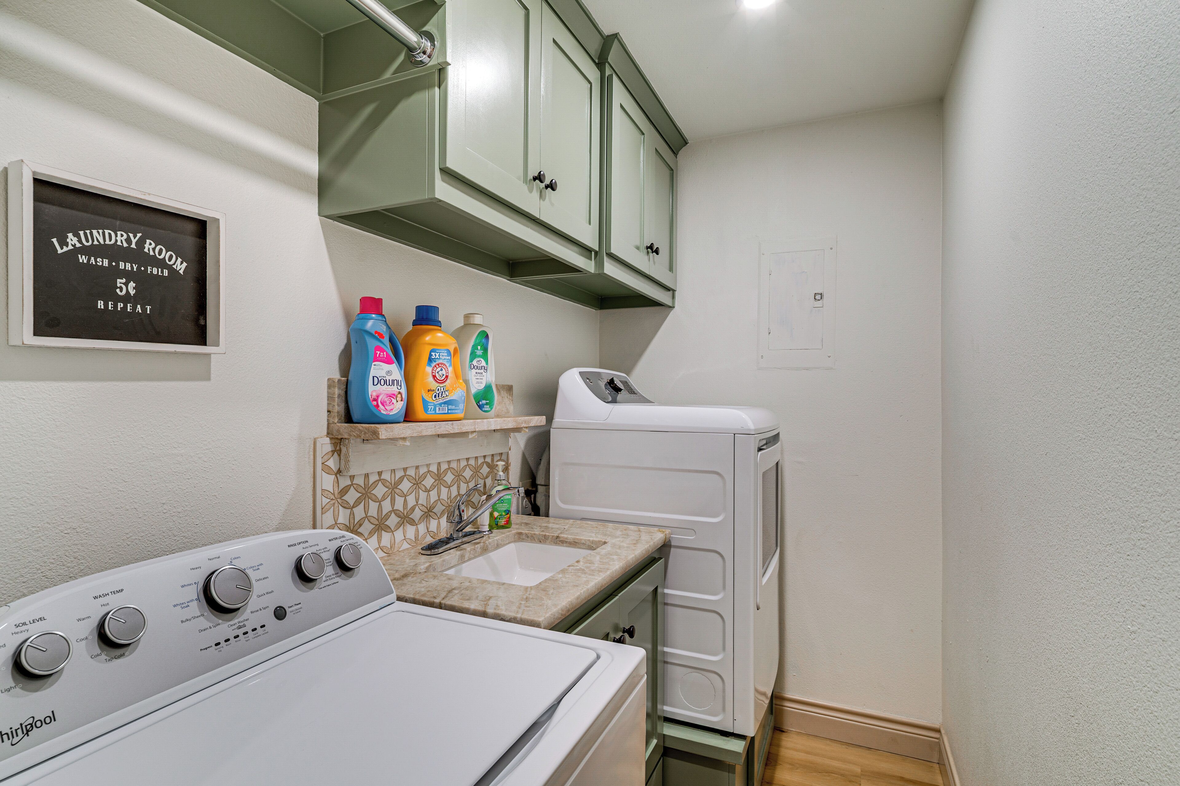 A laundry room with a Whirlpool washer, a sink, and green cabinets above.