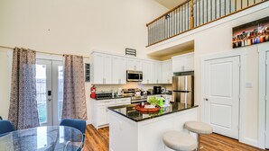 A modern kitchen with white cabinets, a central island, a dining table with chairs, and a staircase leading to an upper level. - Walk to Historic Dtwn: Mckinney Family Retreat (McKinney)