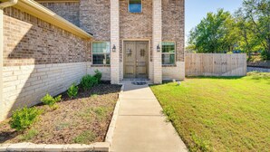 A two-story brick house with a front entrance, a small window above the door, and a wooden fence in the yard. - Walk to Historic Dtwn: Mckinney Family Retreat (McKinney)