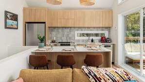 A modern kitchen with wooden cabinets, a central island, and pendant lighting. - La Selva - Intimate getaway & river access (Sainte-Béatrix)