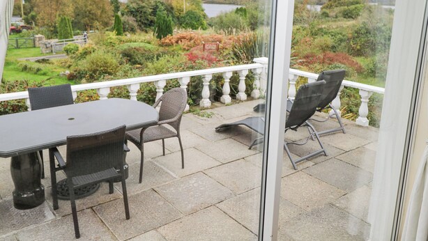 A balcony with a table and chairs, overlooking a scenic landscape with trees and a body of water.
