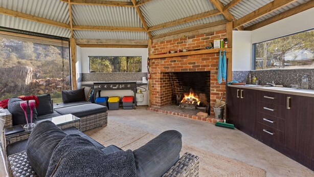 A cozy outdoor living area with a brick fireplace, seating, and a kitchen counter.