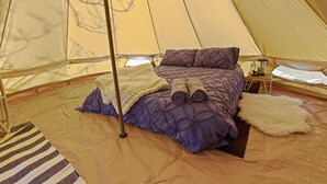 A tent with a bed, pillows, a blanket, and a small table with a kettle.