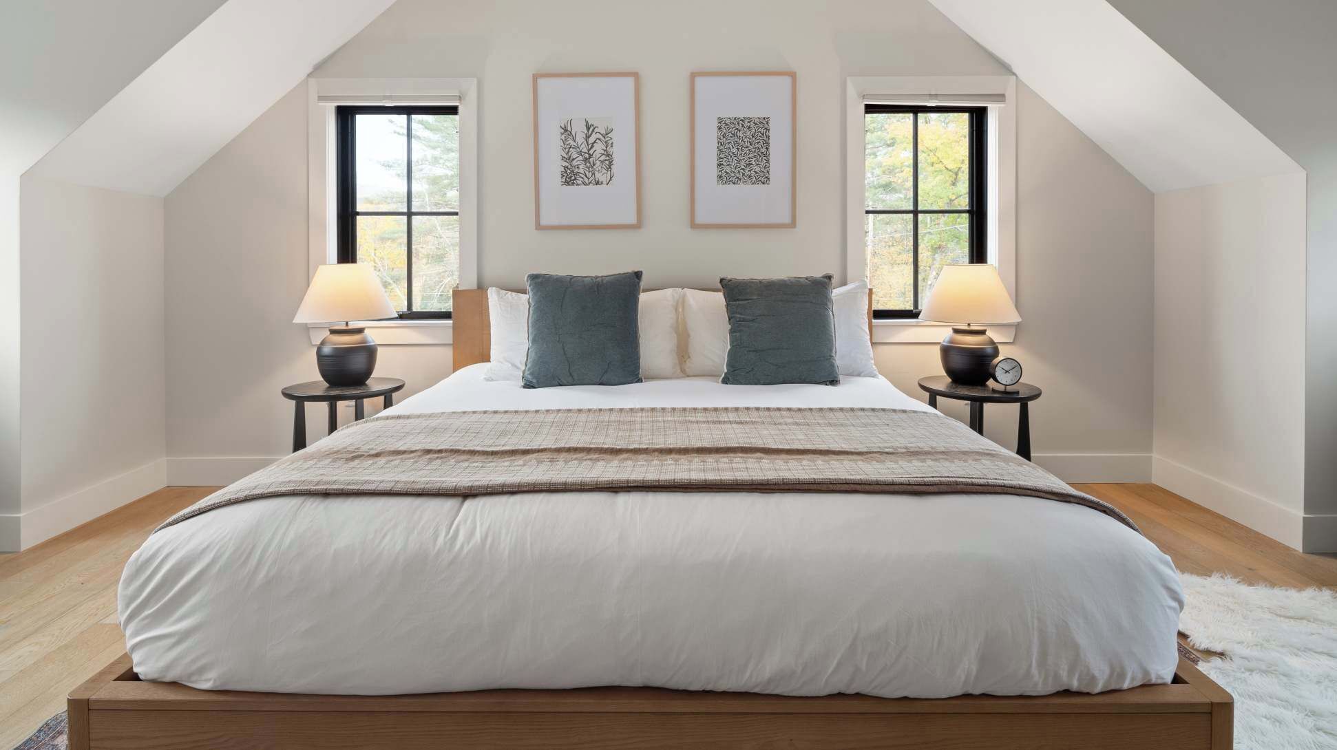 Une chambre à coucher avec un grand lit, deux tables de chevet avec des lampes et deux œuvres d’art encadrées accrochées au mur.