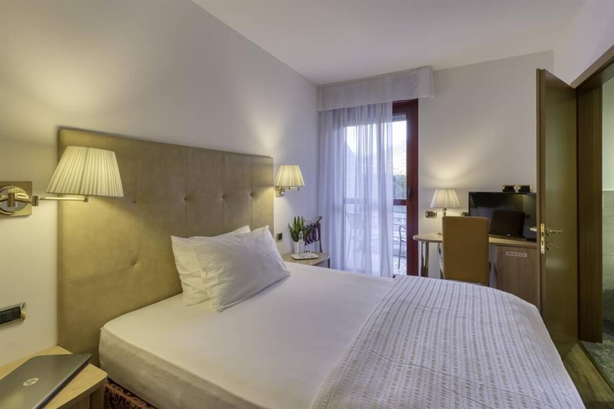 A hotel room with a large bed, two bedside lamps, a desk with a computer, a TV, and a wardrobe.