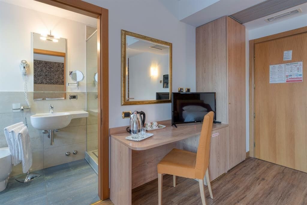 Une salle de bain moderne avec un lavabo, un miroir et des toilettes. On y trouve un bureau en bois avec une chaise et un ordinateur.