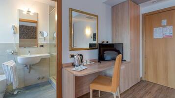 Een moderne badkamer met een wastafel, spiegel en toilet. Er is een houten bureau met een stoel en een computer.