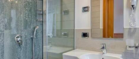 Un baño moderno con ducha envuelta en vidrio, un lavamanos blanco y un espejo sobre él.