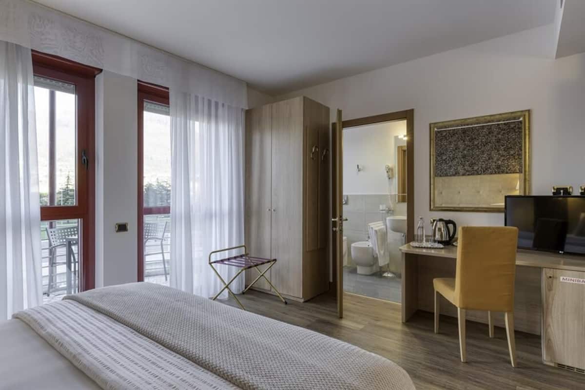 A hotel room with a bed, a desk, a chair, and a view of the outside.