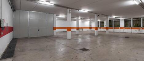 Un grand parking souterrain vide, aux murs blancs et orange, au sol en béton et éclairé par des néons.