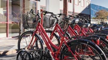 Eine Reihe roter Fahrräder vor einem Gebäude mit großen Fenstern, im Hintergrund ein Berg.