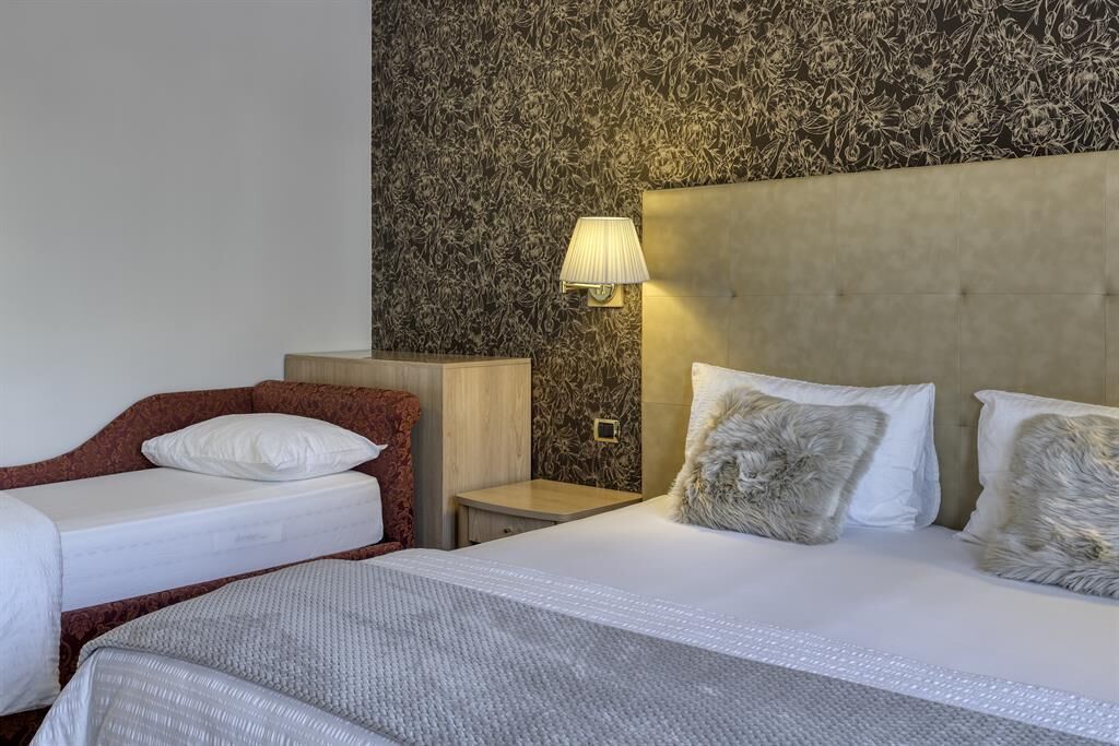 Une chambre d’hôtel avec deux lits, une tête de lit, une table de chevet et un mur orné d’un motif floral.