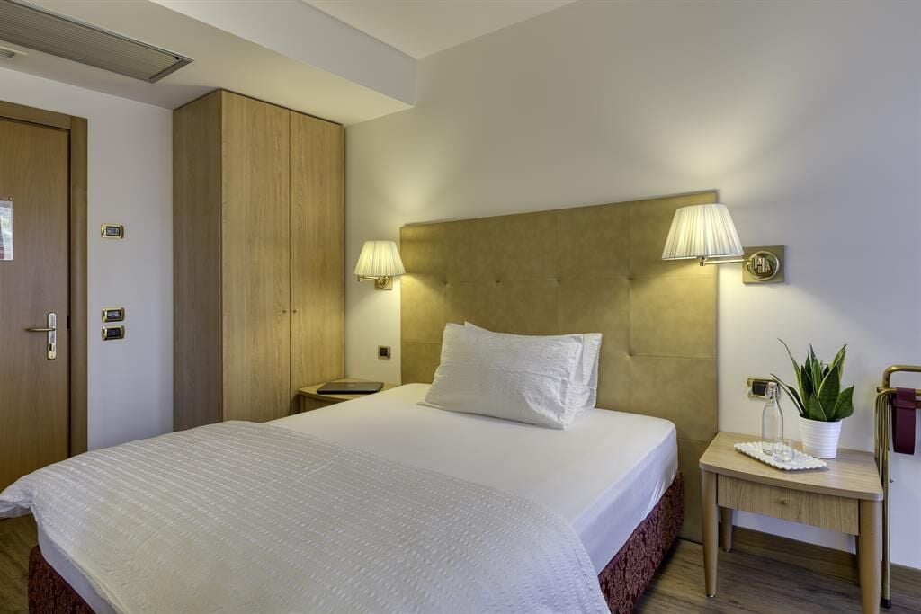 Habitación de hotel con una cama grande, armario de madera, lámparas de noche, una mesita con una planta y una mesilla.