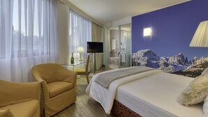 A hotel room with a bed, a chair, a TV, and a bathroom visible through an open door. - Hotel Sporting Trento (Trento)