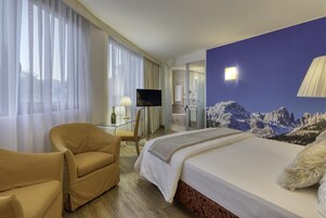Habitación de hotel con cama, una silla, televisor y baño visible a través de una puerta abierta.