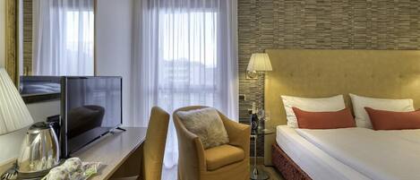 A hotel room with a bed, a desk with a TV, a chair, a coffee maker, and a bottle of champagne.