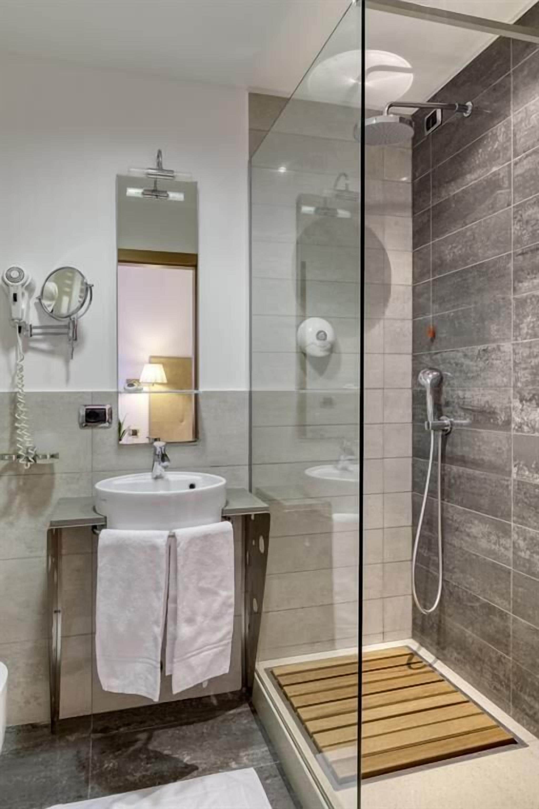 A modern bathroom with a glass shower enclosure, a sink with a mirror, and a towel rack.