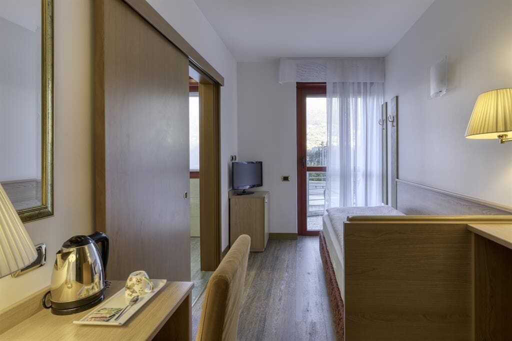 Een hotelkamer met een houten bureau, een televisie, een waterkoker en een bed.