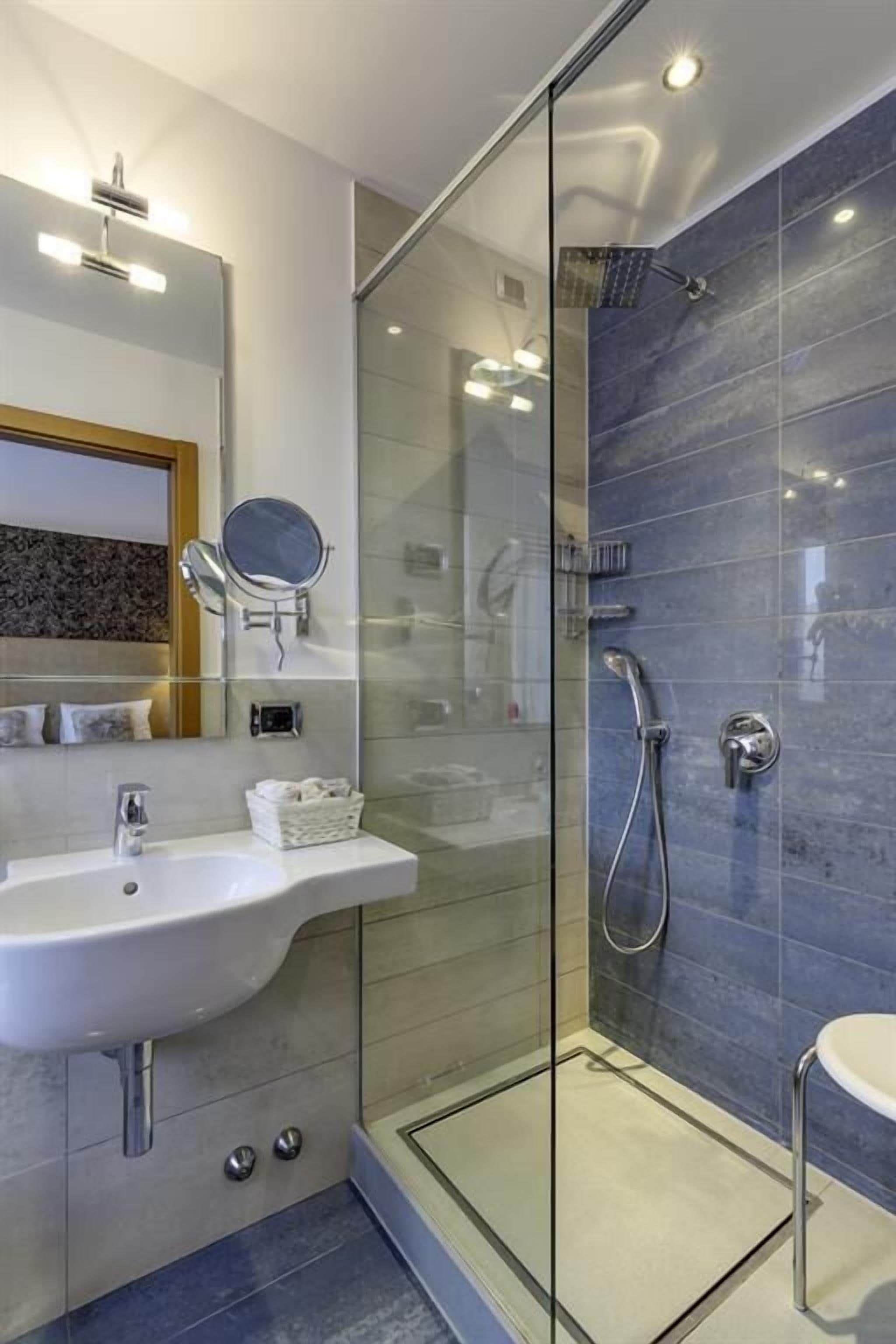 Ein modernes Badezimmer mit einer Duschkabine aus Glas, einem weißen Waschbecken und einem Spiegel.