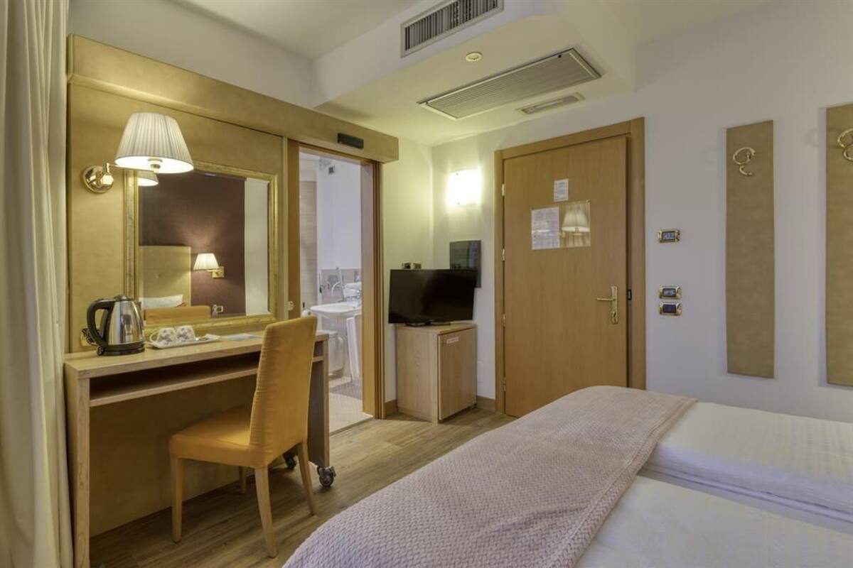 A hotel room with a bed, a desk with a chair, a television, and a bathroom visible through an open door.