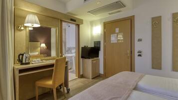 A hotel room with a bed, a desk with a chair, a television, and a bathroom visible through an open door.