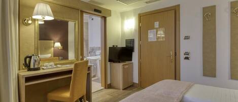 Habitación de hotel con cama, escritorio con silla, televisor y baño visible a través de una puerta abierta.