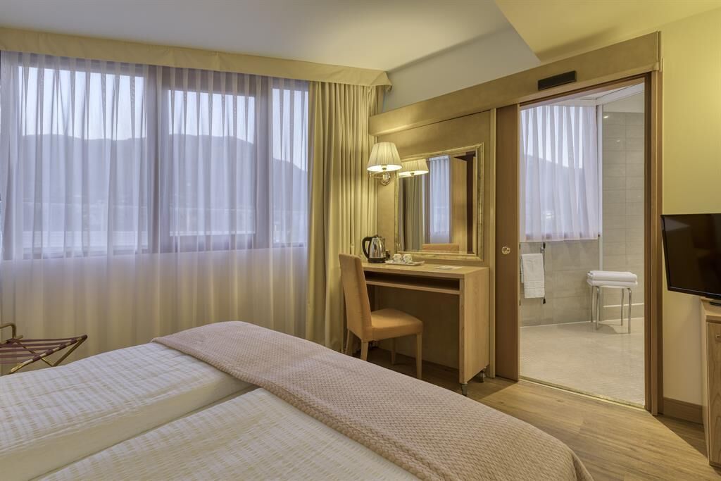 Habitación de hotel con dos camas, un escritorio, una silla, un televisor y un baño visible a través de una puerta abierta.