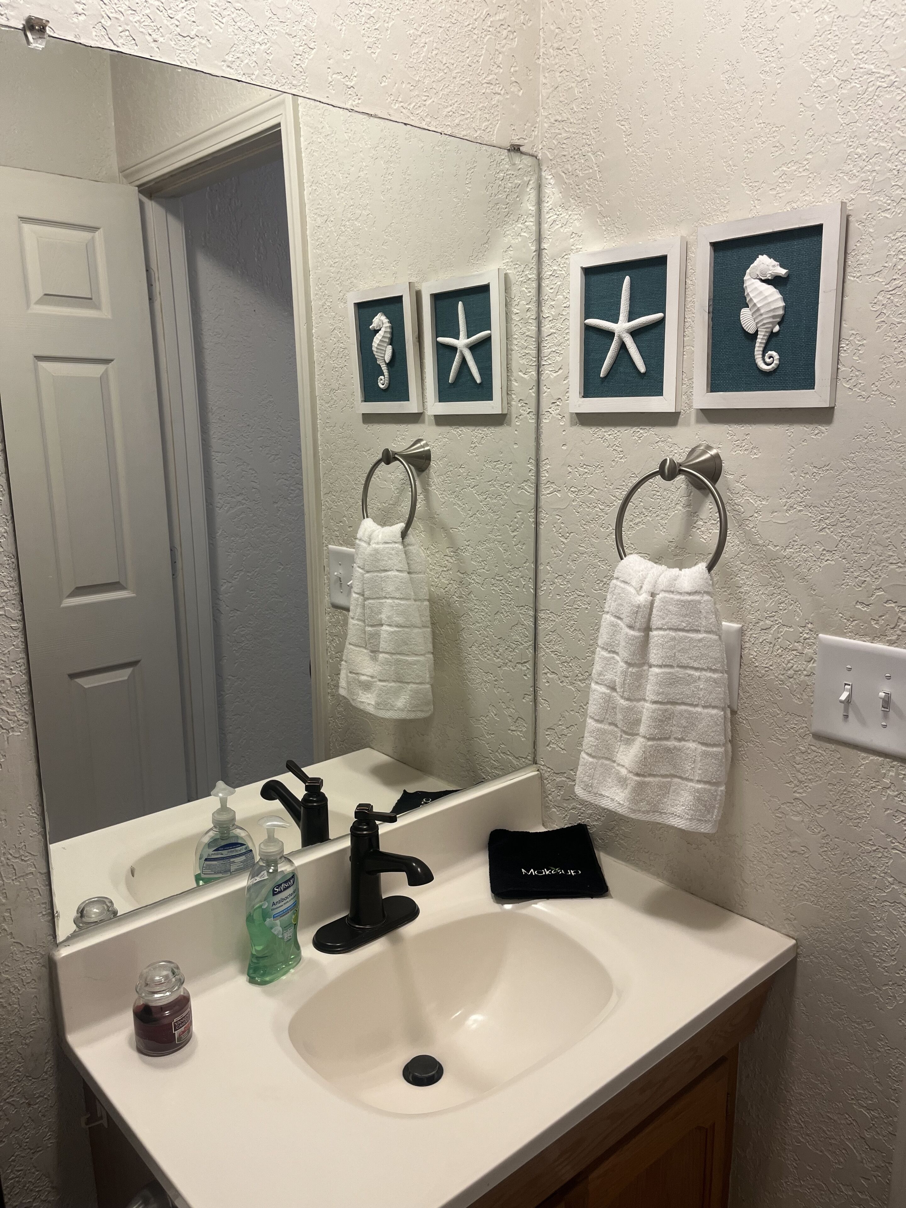 Un baño con lavamanos blanco, grifo negro y espejo. Hay tres cuadros enmarcados en la pared, y dos toallas colgadas en aros.