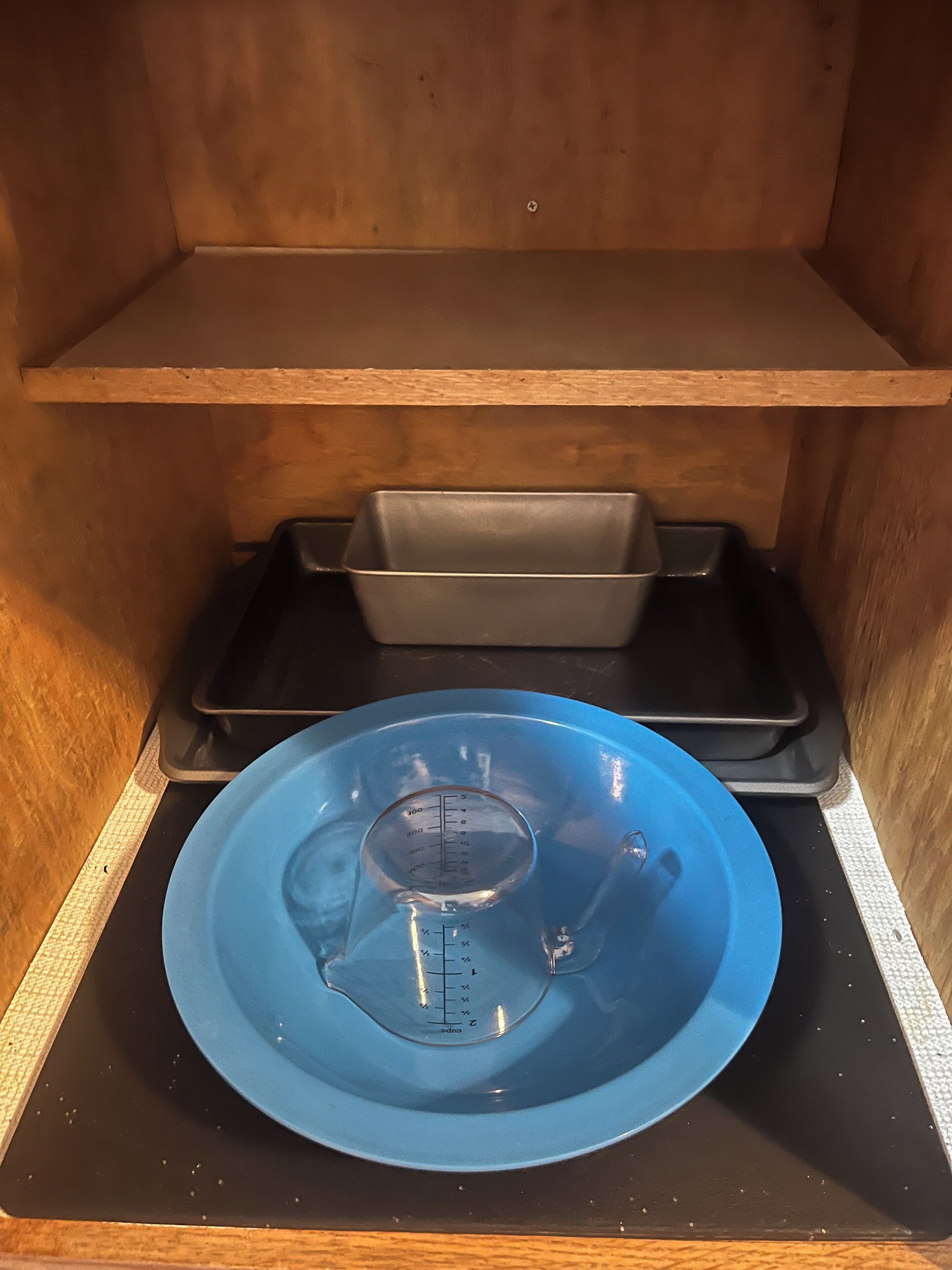 Eine Küche mit einer blauen Rührschüssel auf einer schwarzen Arbeitsplatte, einer schwarzen Ablage und einem Holzregal darüber.
