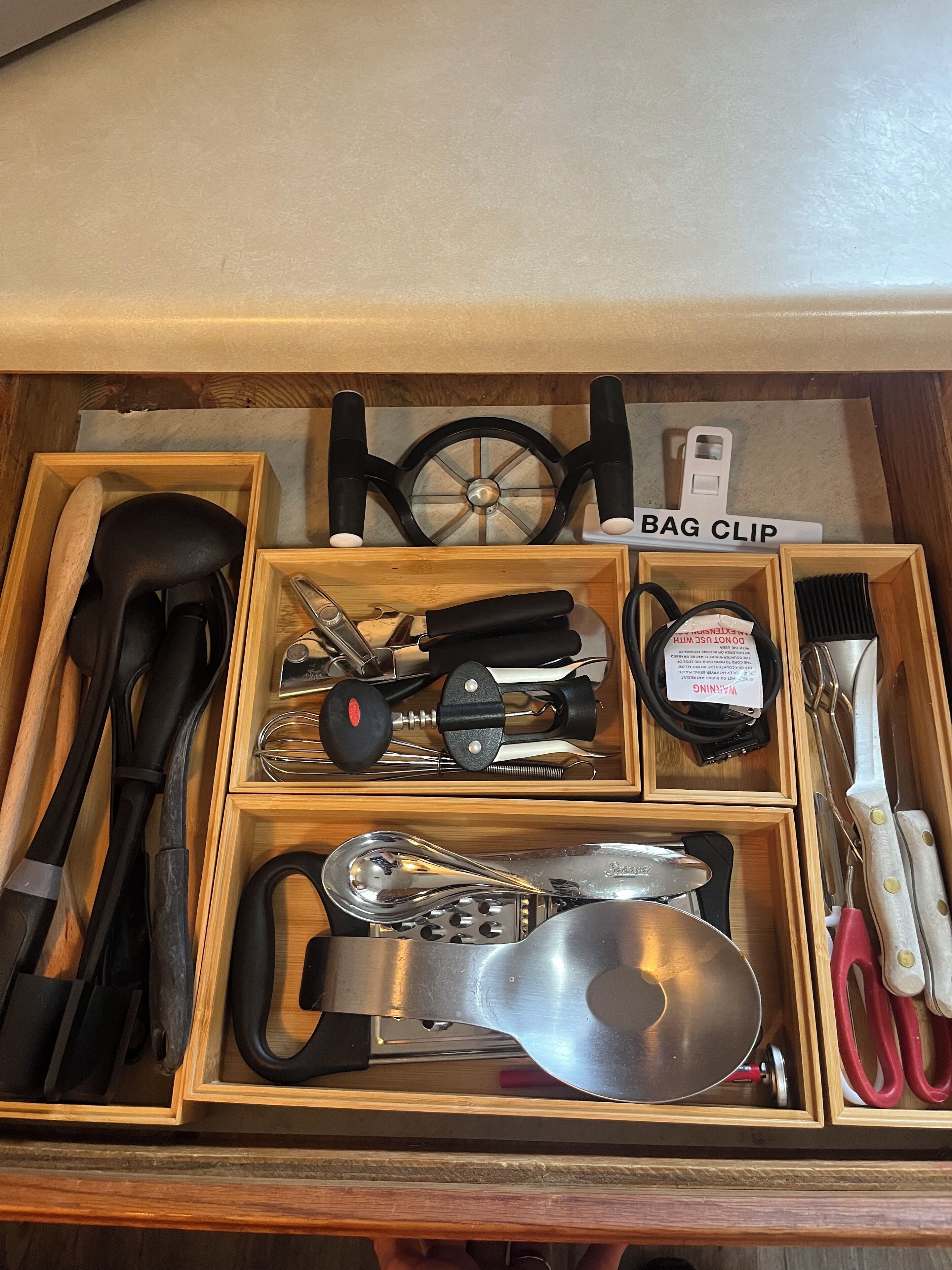 Un cajón con diversos utensilios y herramientas de cocina, incluyendo un batidor, un cierre para bolsas y una cuchara.