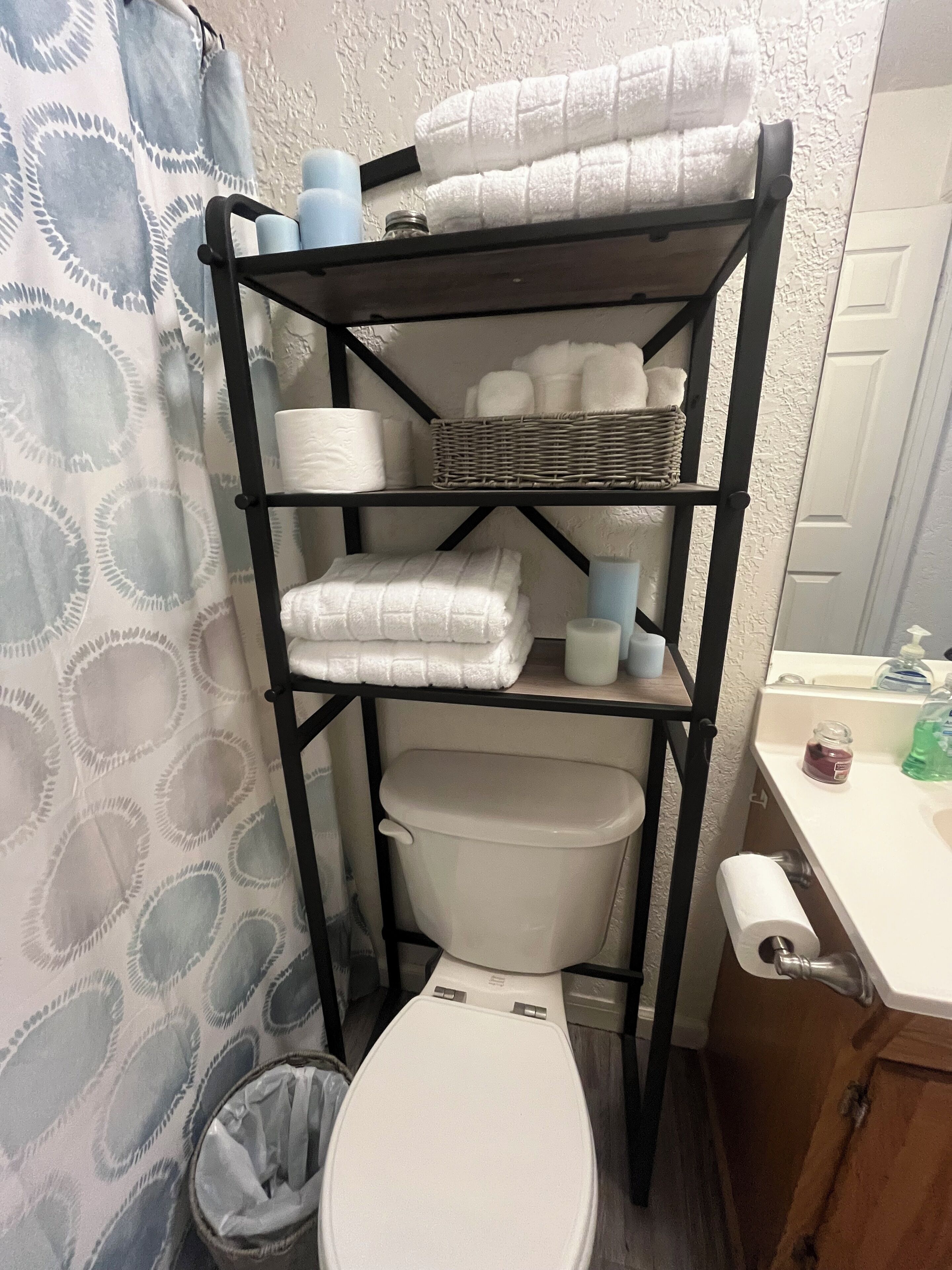 Une salle de bain avec des toilettes, une étagère avec des serviettes et un panier.
