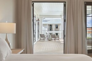A hotel room with a bed, a nightstand, a lamp, and a view of a balcony with chairs and a table.
