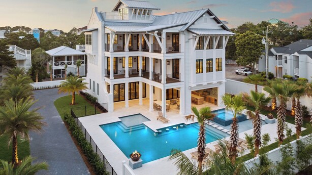 Une grande maison à plusieurs étages, dotée d’une piscine, entourée de palmiers et d’une pelouse bien entretenue.
