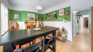 Et spiseområde med et sort bord, stole og en bænk. Væggen er dekoreret med reoler, planter og pynteting.