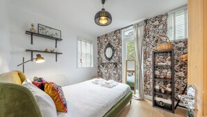 Et pænt indrettet soveværelse med seng, hylder med pynteting, en hængende lampe og væg med blomstermønster.
