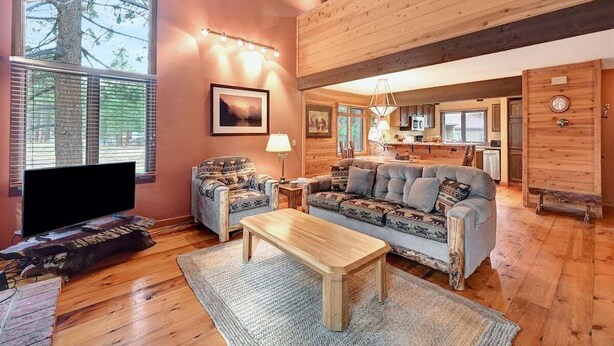 A cozy living room with a sofa, a coffee table, and a television. There is a window with blinds and a picture frame on the wall. - Wildflower 62: Nice Condo, Close to the Green Line (Mammoth Lakes)