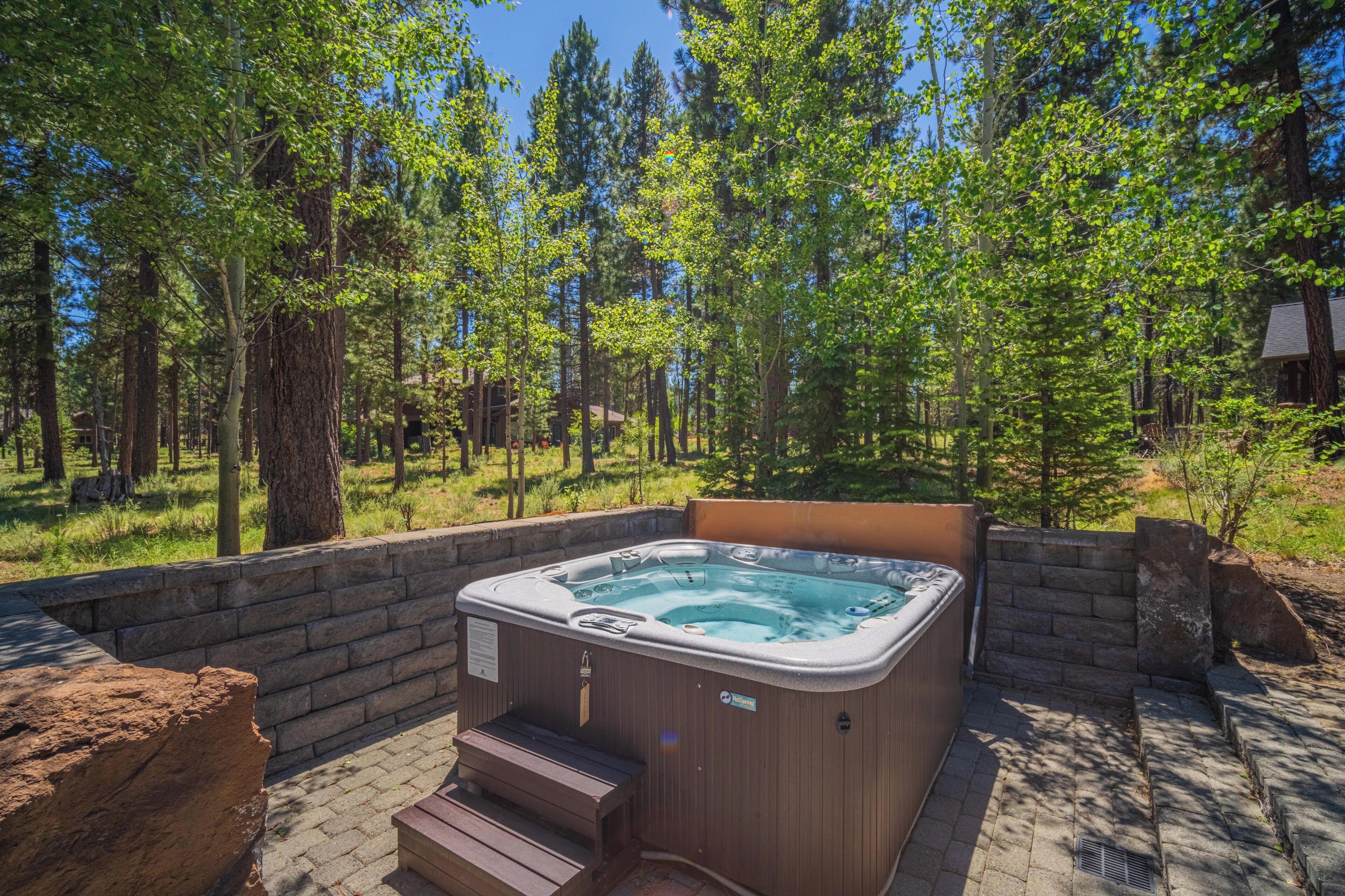 A hot tub in a forested area with a stone wall and steps leading up to it.