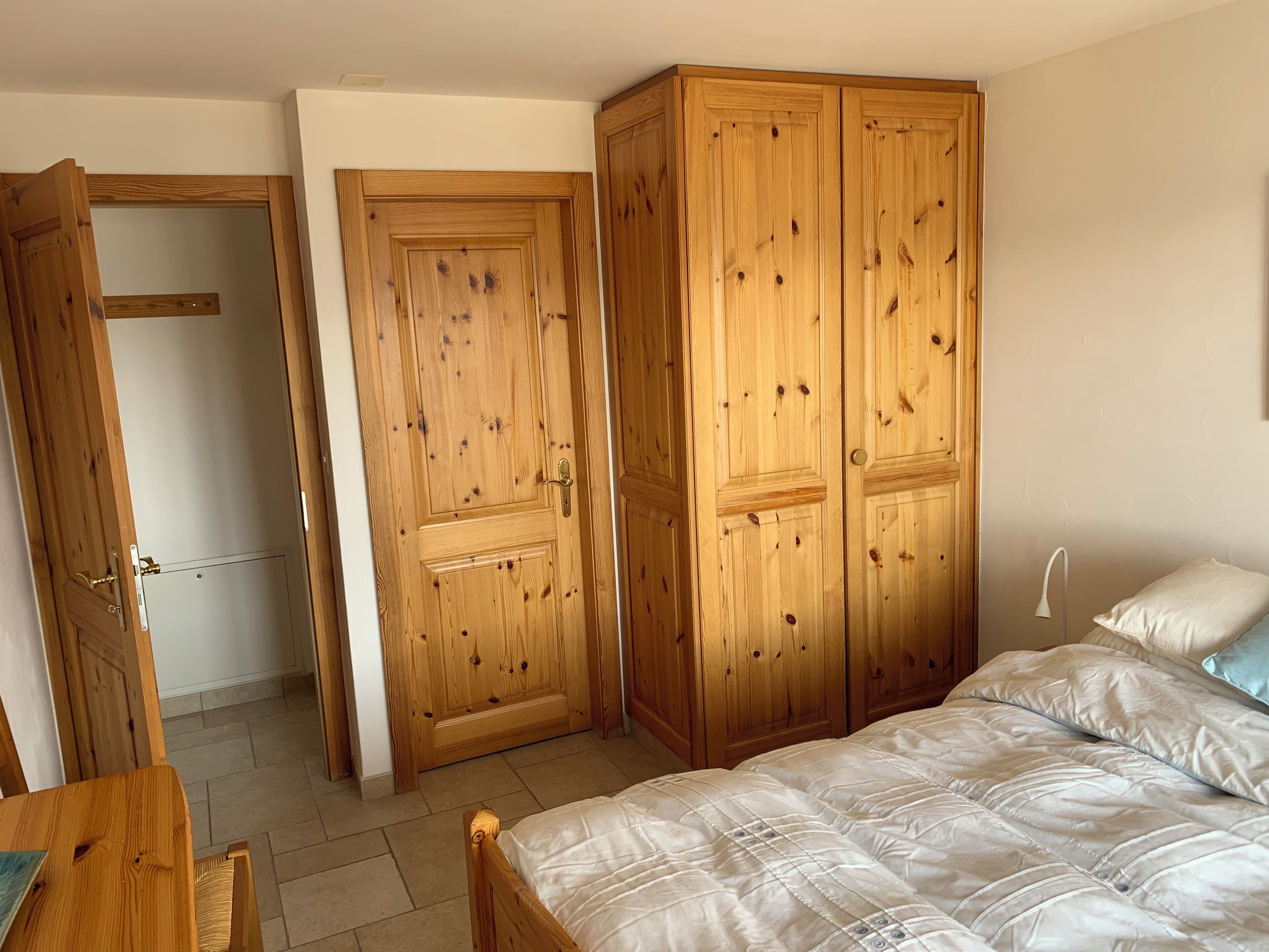 A bedroom with a bed, wooden wardrobe, and a door.