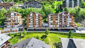 A cluster of multi-story buildings with balconies, surrounded by lush greenery and a mountainous backdrop. - 3 Bedroom Apartment Nendaz, Switzerland. 5 mins walk to tracouet gondala. (Nendaz)