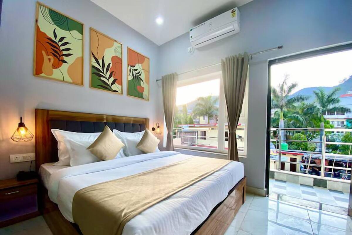 A hotel room with a bed, a nightstand, a wall-mounted air conditioner, and a window with curtains.