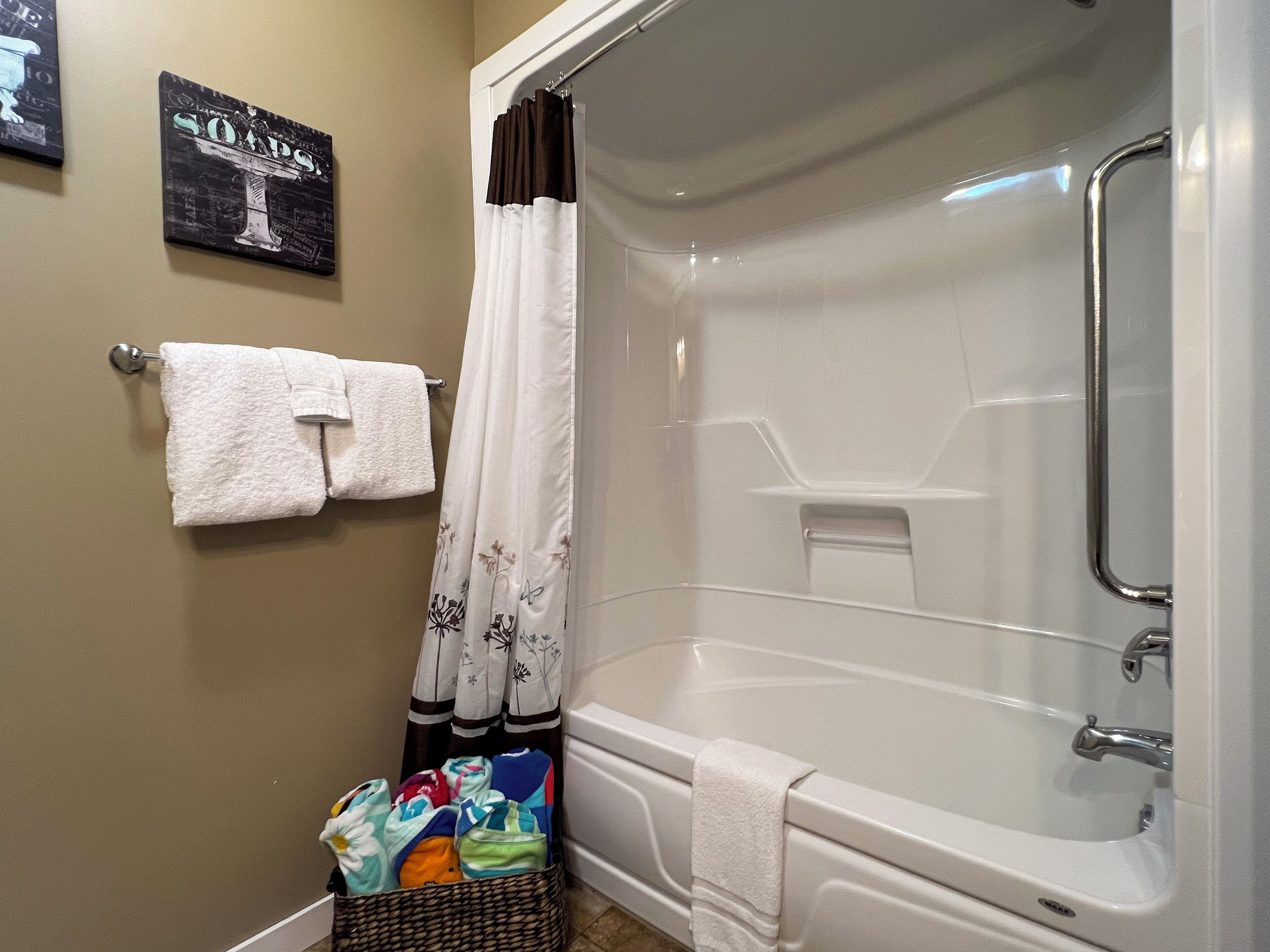 A bathroom with a bathtub, a shower curtain, a towel rack, and a basket of towels.