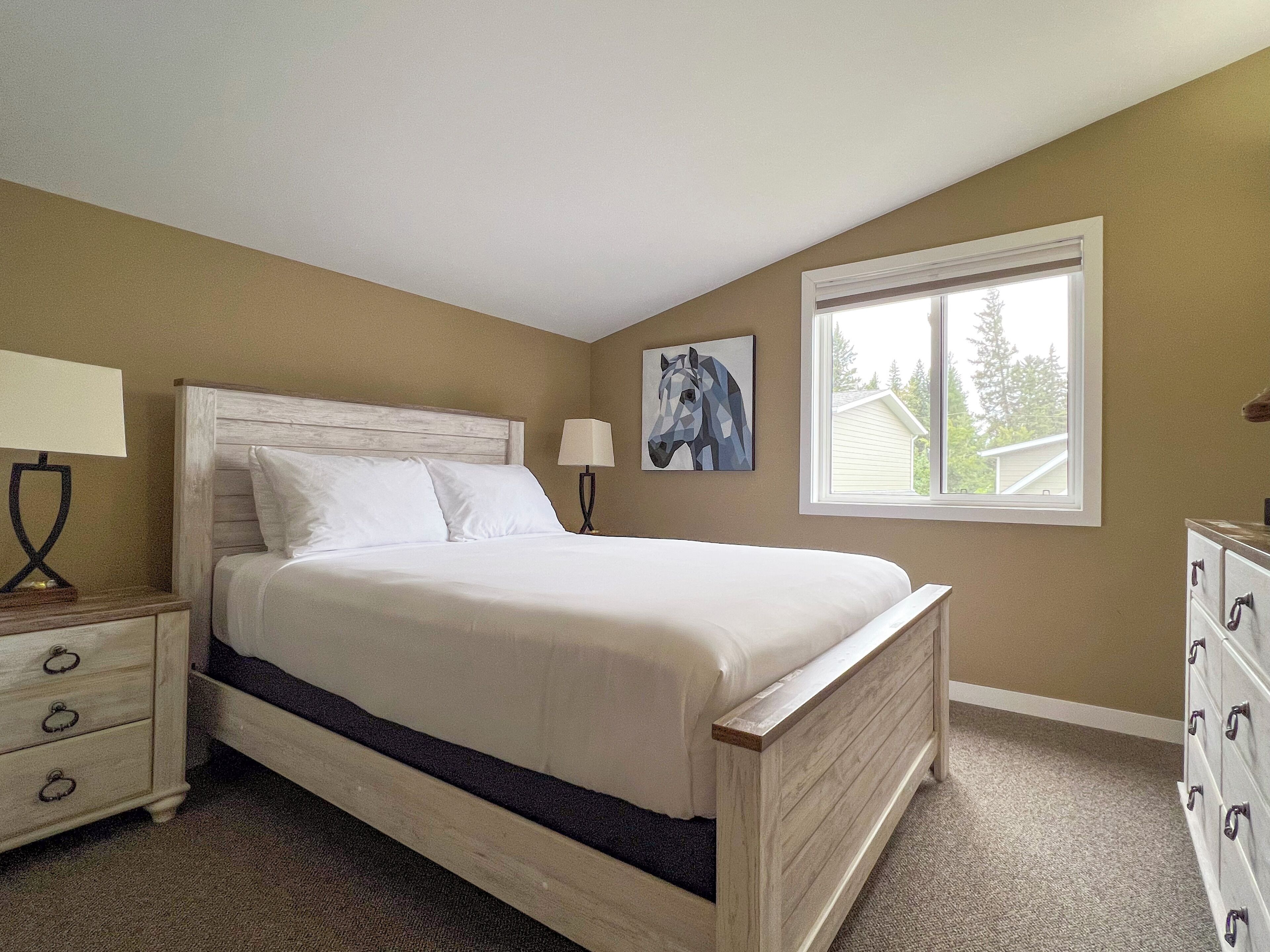 A bedroom with a bed, nightstand, dresser, and a window with a view of a house.