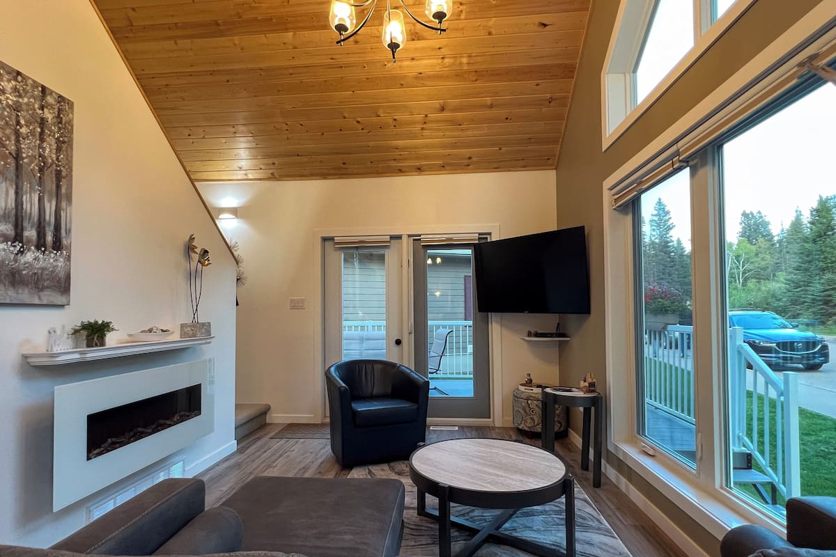 A living room with a fireplace, a television, and a large window overlooking a deck.