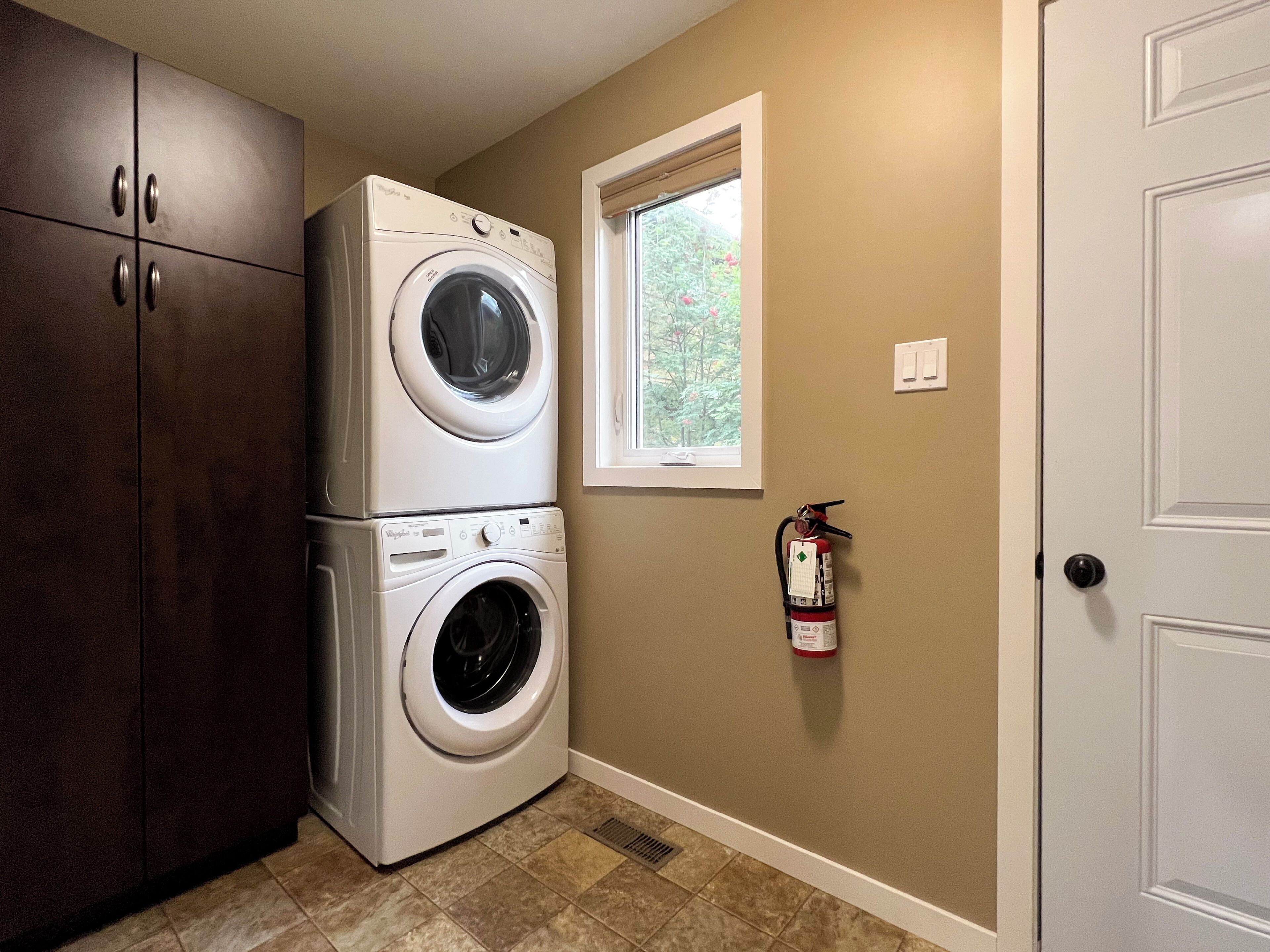 A laundry room with stacked washers and dryers, a window, a fire extinguisher, and a door.