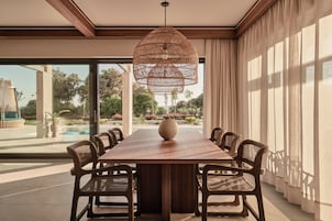 Un comedor con una larga mesa de madera, seis sillas de mimbre, un jarrón grande y una lámpara colgante de fibras naturales.