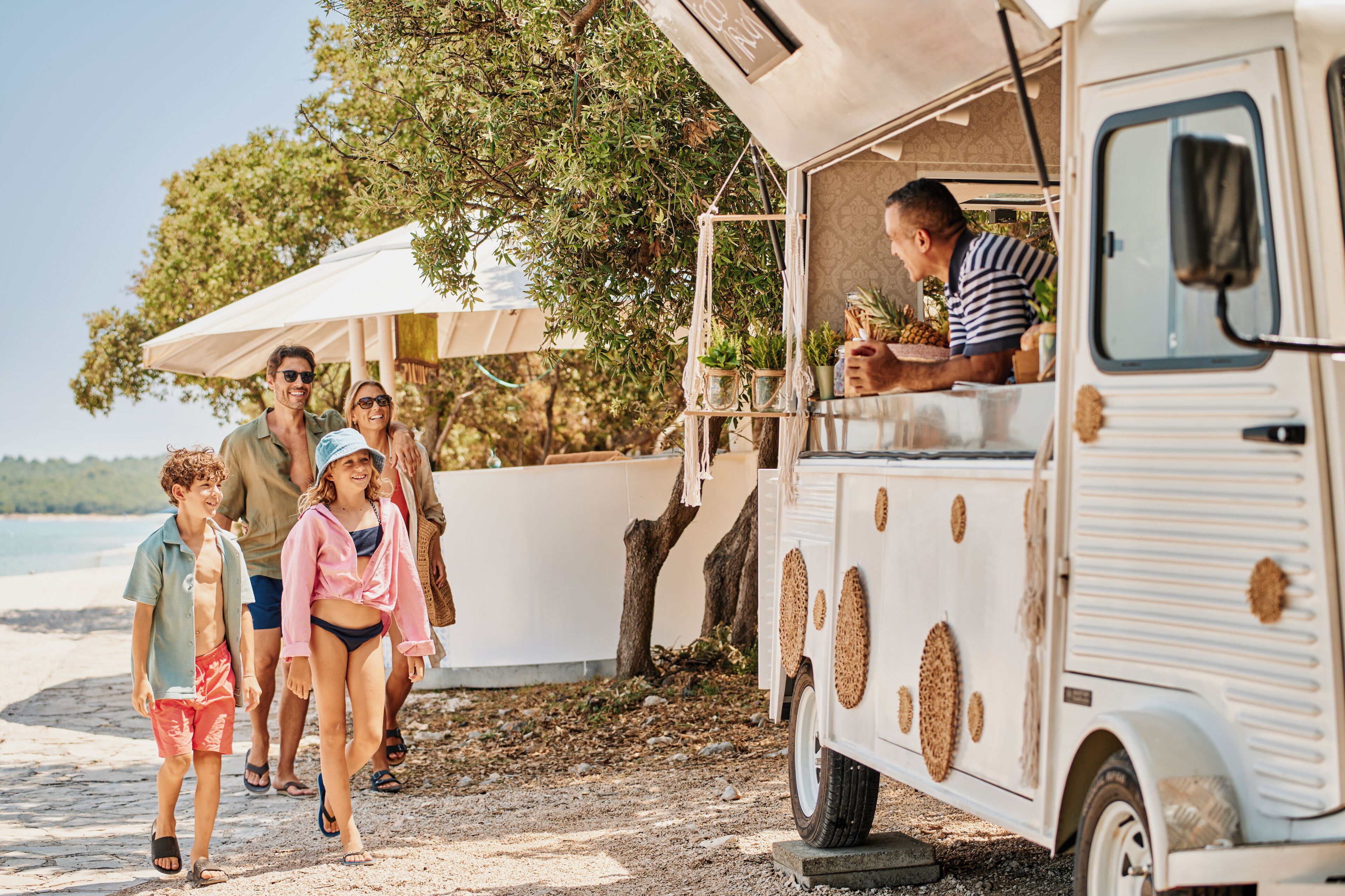 Un camión de comida de estilo vintage estacionado en una playa, con un grupo de personas caminando cerca.