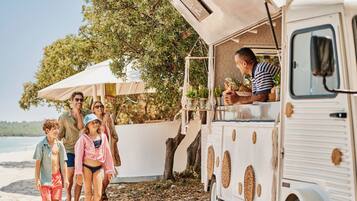 Un camión de comida de estilo vintage estacionado en una playa, con un grupo de personas caminando cerca.