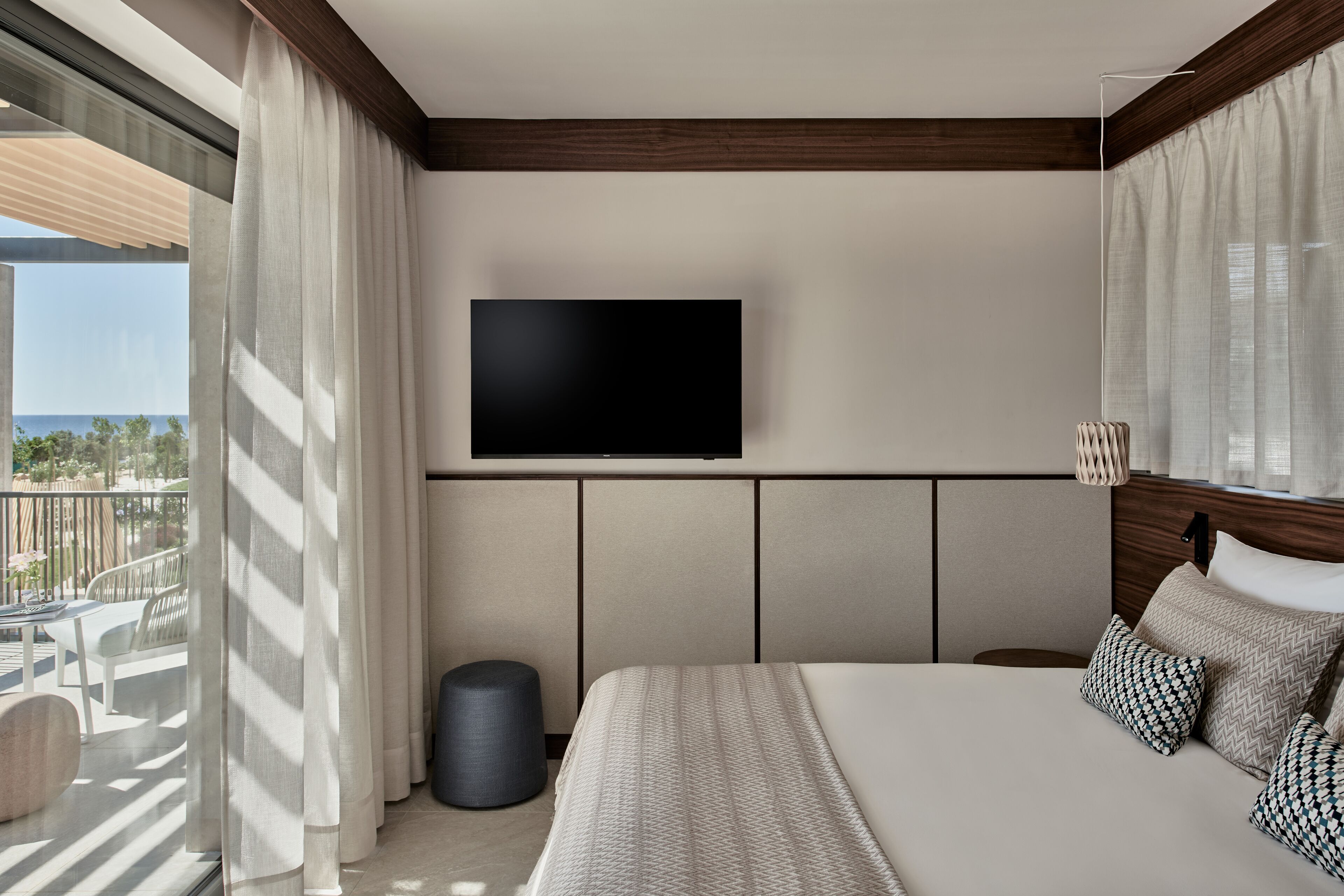 Una habitación de hotel moderna con una cama grande, un televisor de pantalla plana en la pared y un balcón con cortinas.