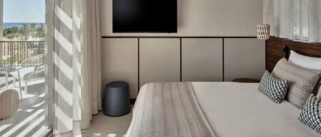 Una habitación de hotel moderna con una cama grande, un televisor de pantalla plana en la pared y un balcón con cortinas.